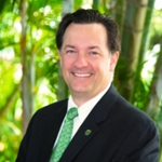 Portrait of a smiling man in a suit and green tie standing in front of green plants